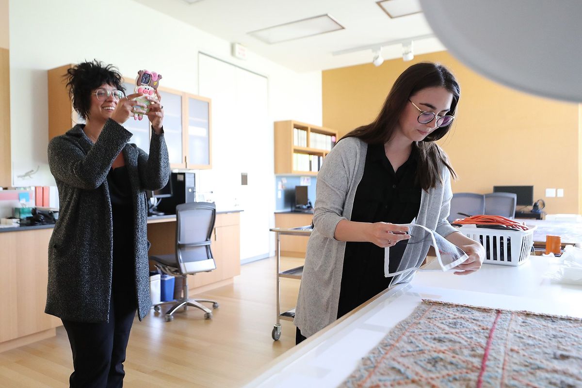 Carolyn Rivera (left), brand engagement manager at the Barnes Foundation, records a video on her phone as AnnaLivia McCarthy, senior conservation coordinator, demonstrates her work in the lab.   (David Maialetti/Philadelphia Inquirer)