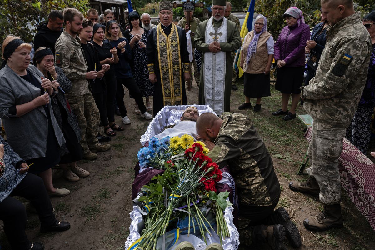 Two brothers, Vladyslav, right, and Konstantin, center, both Ukrainian soldiers, are joined by loved ones as they say goodbye to their oldest brother, Mikhailo Smyuha, who was also a Ukrainian soldier, during his funeral in Kalynivka, Ukraine, on Sunday.  (LYNSEY ADDARIO)