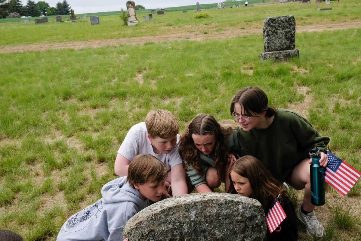 Orchard Prairie students Abram Sutton, left, Ben Borders, Brooklynn Booth, Maddy Weeks and Abigail Wortmann gather around a grave Thursday as they work to clean up Orchard Prairie Cemetery and place flags next to the graves of veterans in Orchard Prairie in observance of Memorial Day.  (Tyler Tjomsland/The Spokesman-Review)