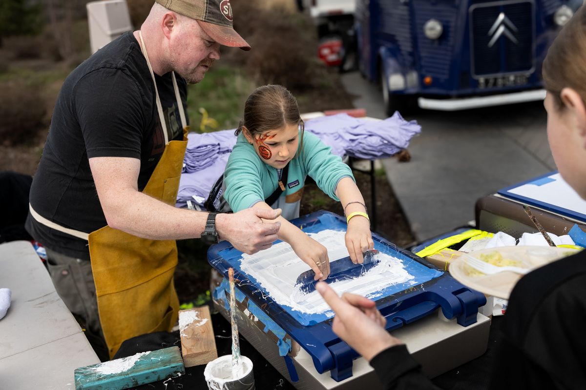Artist Chris Bovey shows Brooklyn Walsh, 9, from Helena, how to screen print her free T-shirt that says, “Spokane Champions Women’s Sports,” during the Fan Fest Block Party on Saturday, March 29. (COLIN MULVANY/THE SPOKESMAN-REVIEW)