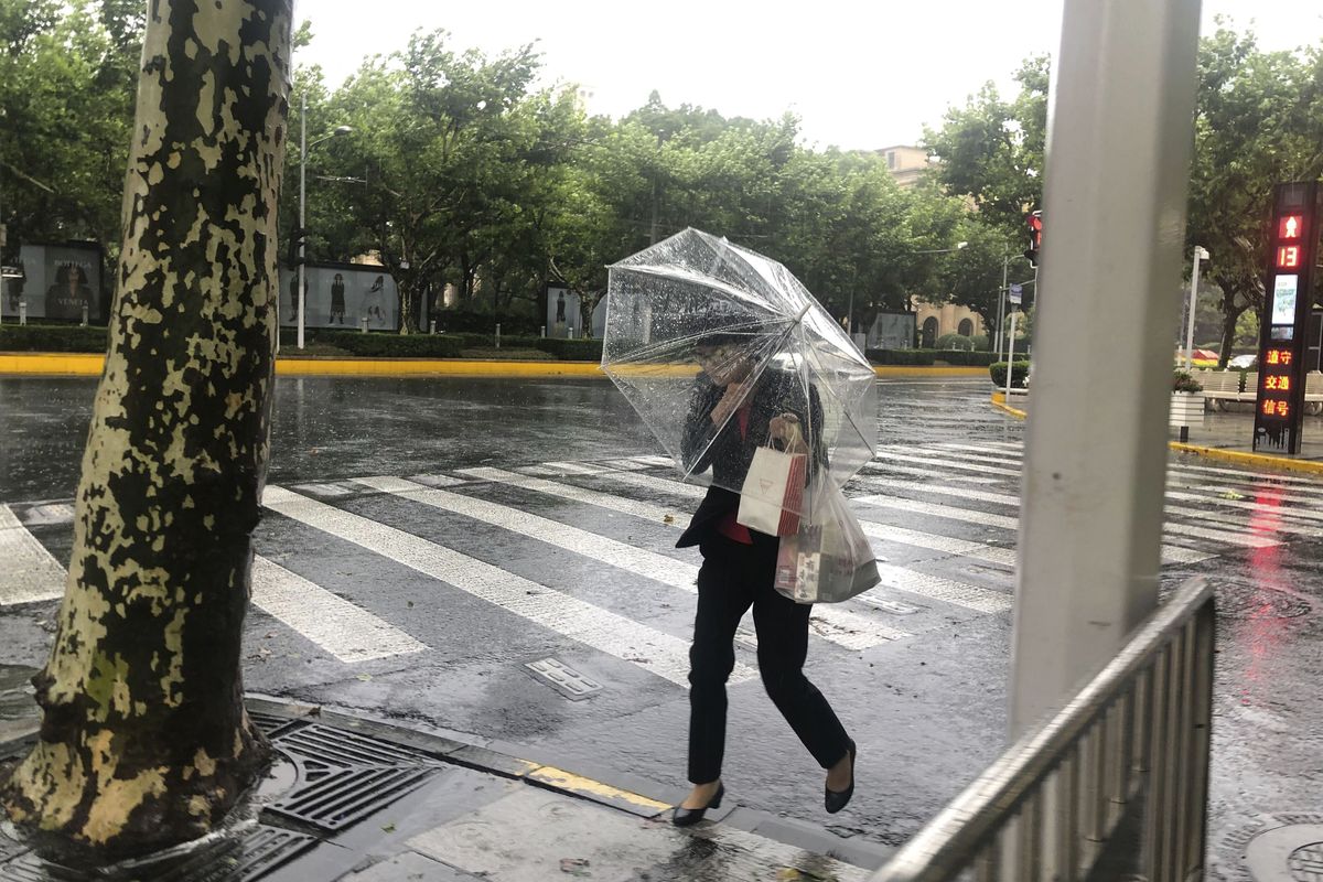 A woman carrying an umbrella braces against the wind and rain Sunday as Typhoon In-fa sweeps through Shanghai, China. Typhoon In-fa hit China’s east coast south of Shanghai on Sunday, and people living near the sea were evacuated. Airline flights and trains were canceled, and the public was ordered to stay indoors.  (Chen Si)
