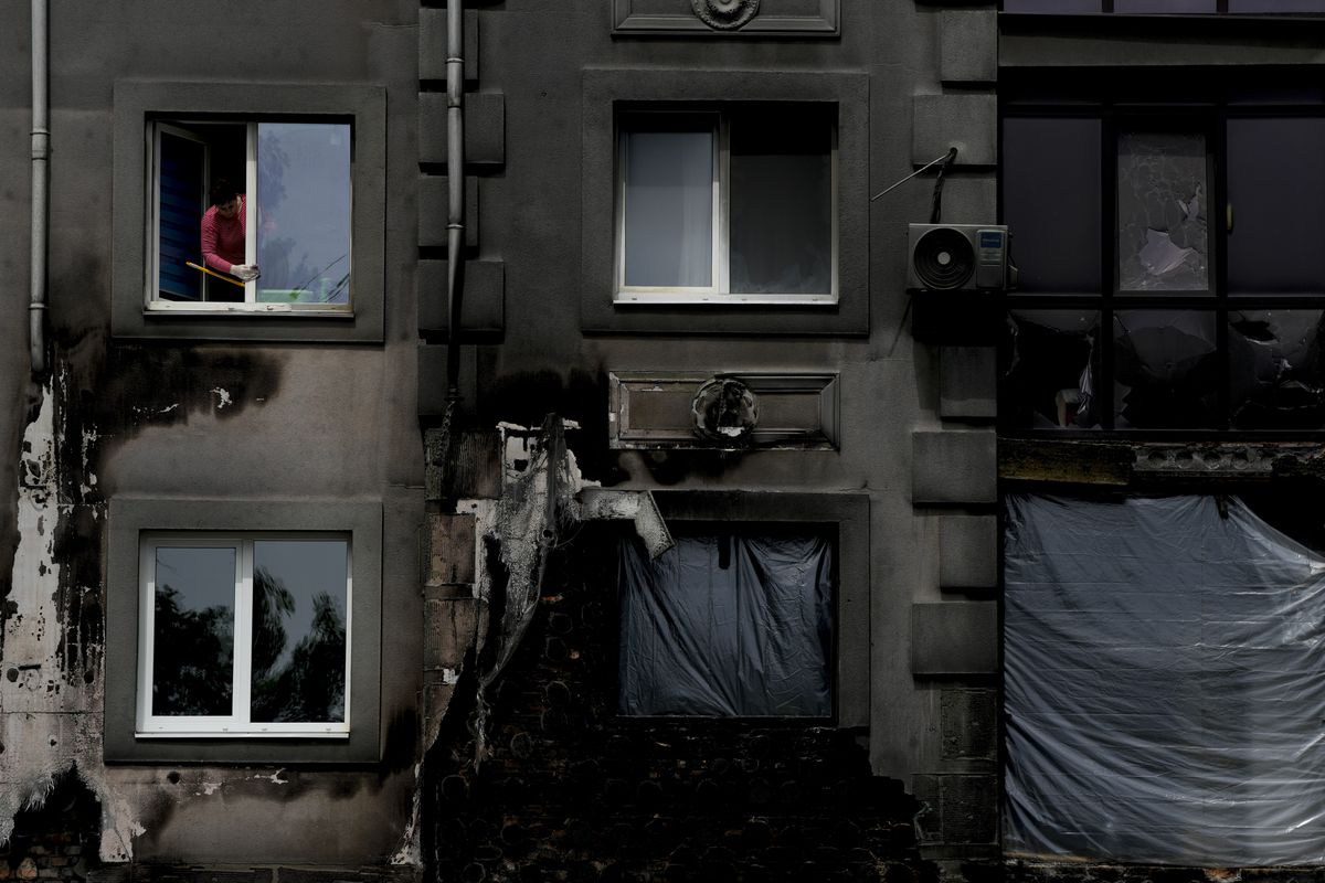 A woman cleans a window of her home ruined by shelling, in Bucha, on the outskirts Kyiv, Ukraine, Wednesday, May 25, 2022.  (Natacha Pisarenko)