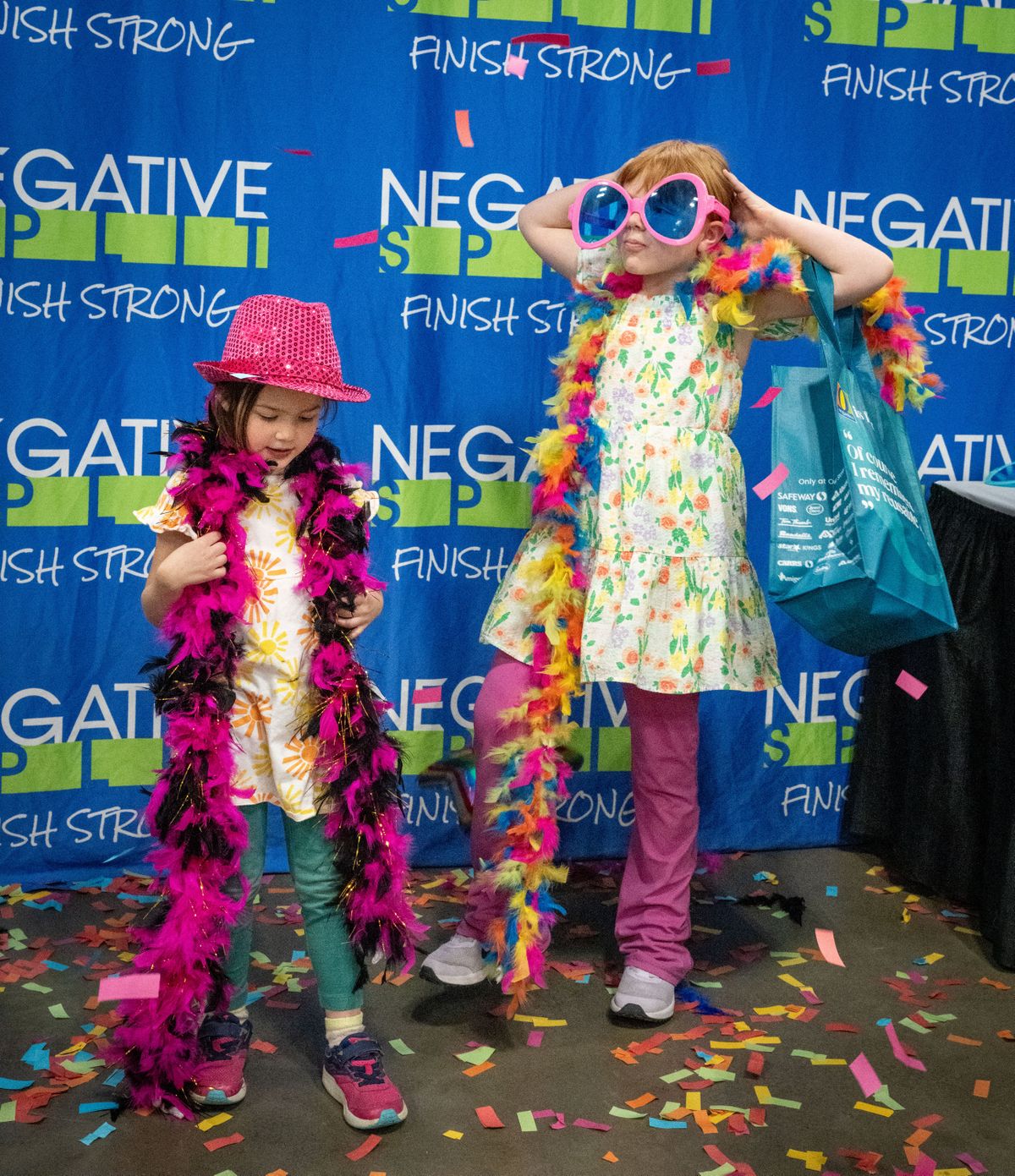 Fiona Jones, 5, on left, and her sister Lilly, 8, dressed in silly accessories, pose for a photo as confetti rains down in the Negative Split booth at the Bloomsday Trade Show, Friday, May 3, 2024. After Bloomsday participants picked up their race packets, they navigated through dozens of vendors selling running gear and other services.  (COLIN MULVANY/THE SPOKESMAN-REVI)