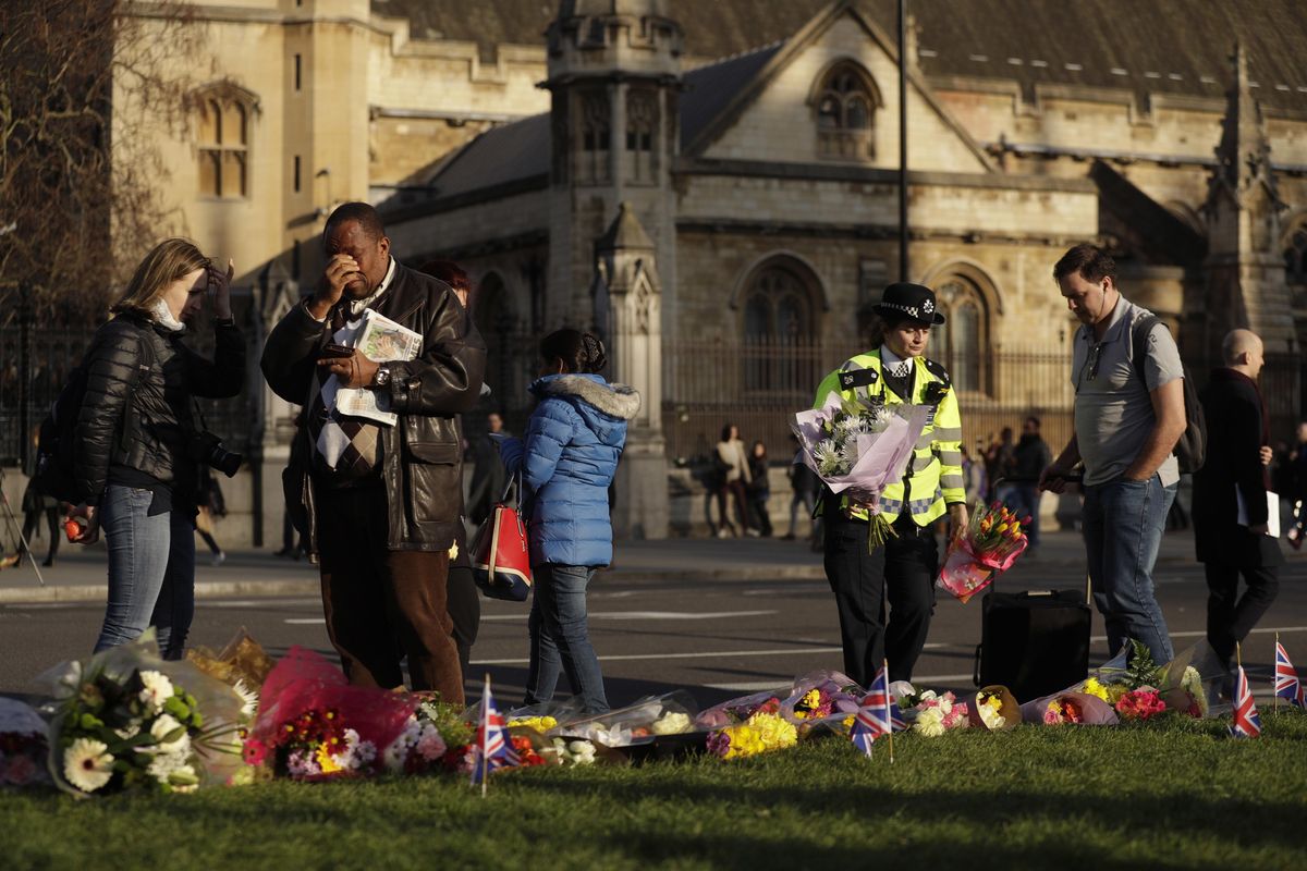 A police officer places flowers as a man gestures beside floral tributes to victims of Wednesday