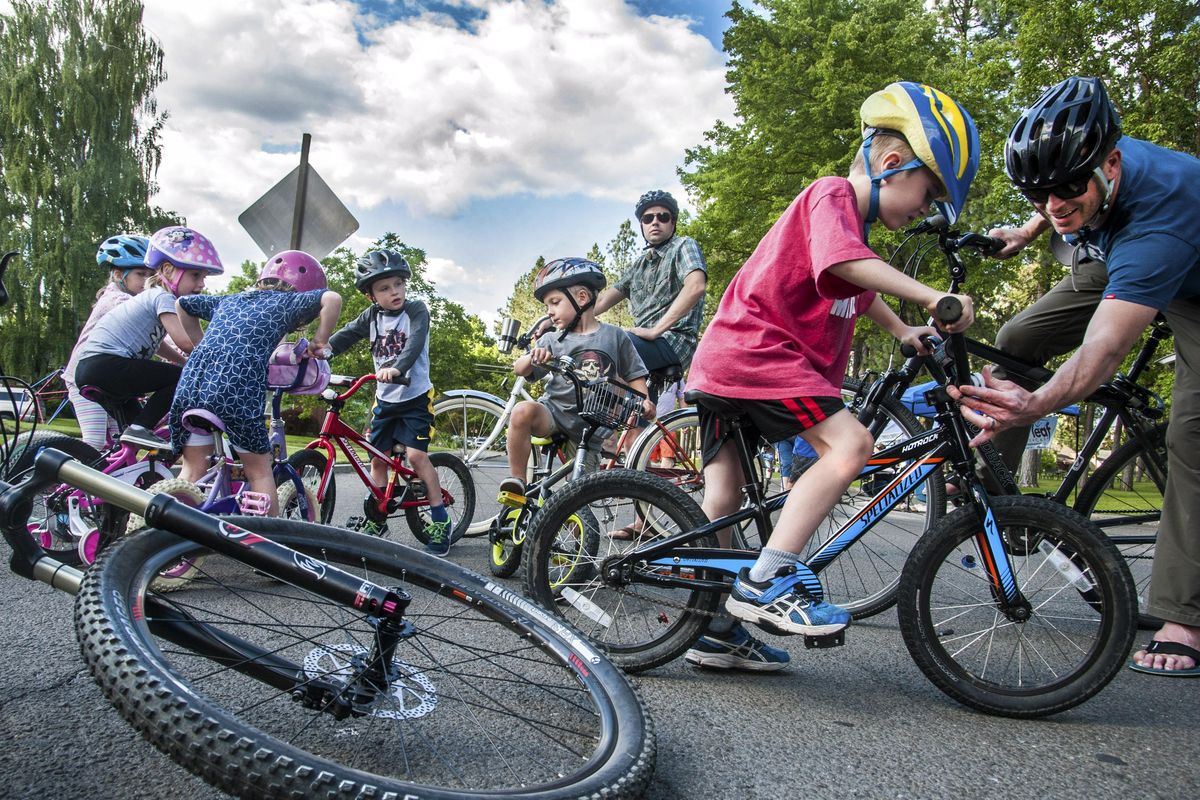 Tim Lyons, right, assists his son Sean, 5, with his safety lights as neighborhood children gather on Post Street near Comstock Park in Spokane to begin their participation in the Summer Parkways on Tuesday. (Dan Pelle / The Spokesman-Review)