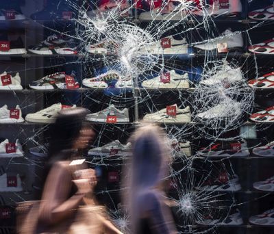 People walk past cracks in a damaged window of a retail store during a clash in Stuttgart, Germany, Sunday, June 21, 2020.   (Marijan Murat)