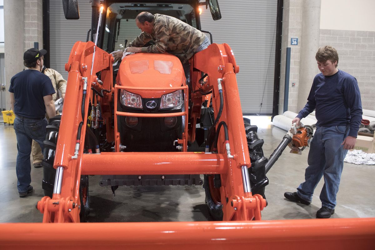 Tom Hutton, center, and his son Talon Hutton, right, wipe down and dry off a Kubota tractor at the Spokane Convention Center after it was washed Sunday, Feb. 5, 2017. All the equipment loading in for the annual Ag Trade Show this week had to be washed, dried off, then polished up for display. Talon is a member of the Cheney Future Farmers of America chapter.  Father and son are volunteering for show preparation. (Jesse Tinsley / The Spokesman-Review)