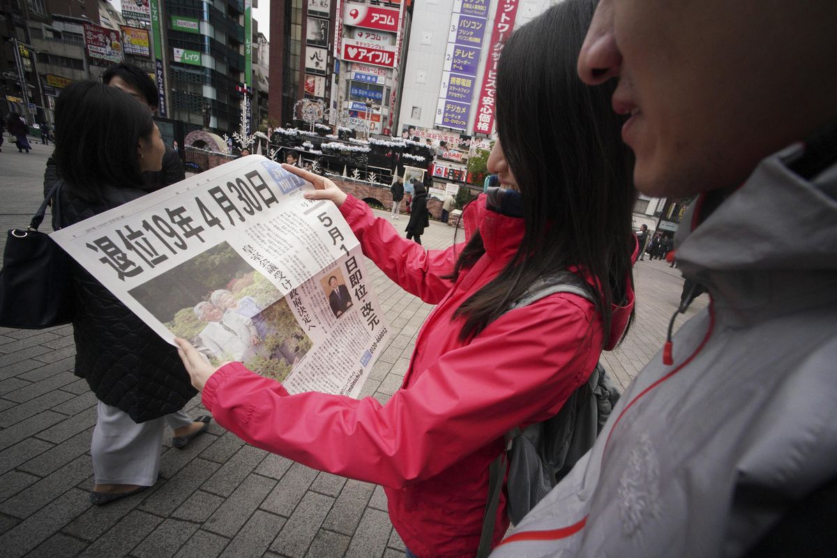 Passers-by read an extra edition of a newspaper reporting about Emperor Akihito to abdicate date, at Shimbashi Station in Tokyo Friday, Dec. 1, 2017. Japan
