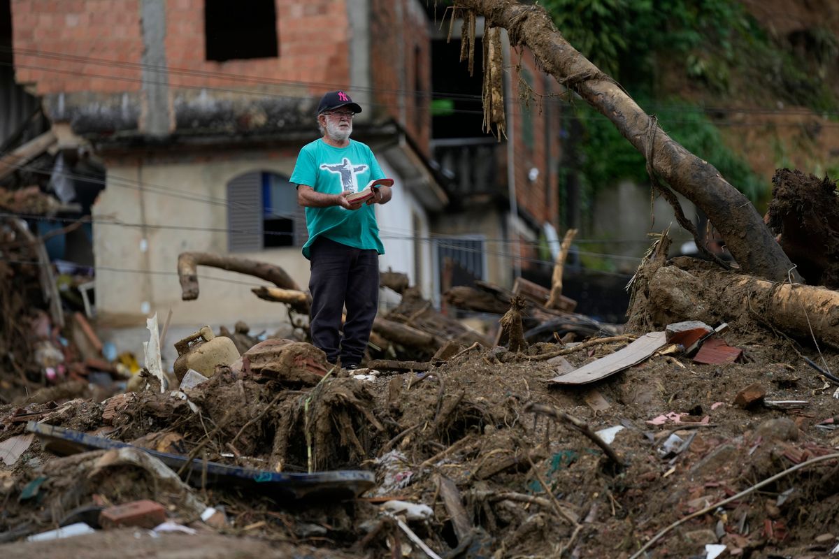 A man with a Bible stands on the debris of homes destroyed by mudslides on the third day of rescue efforts in Petropolis, Brazil, Friday, Feb. 18, 2022. (Silvia Izquierdo)