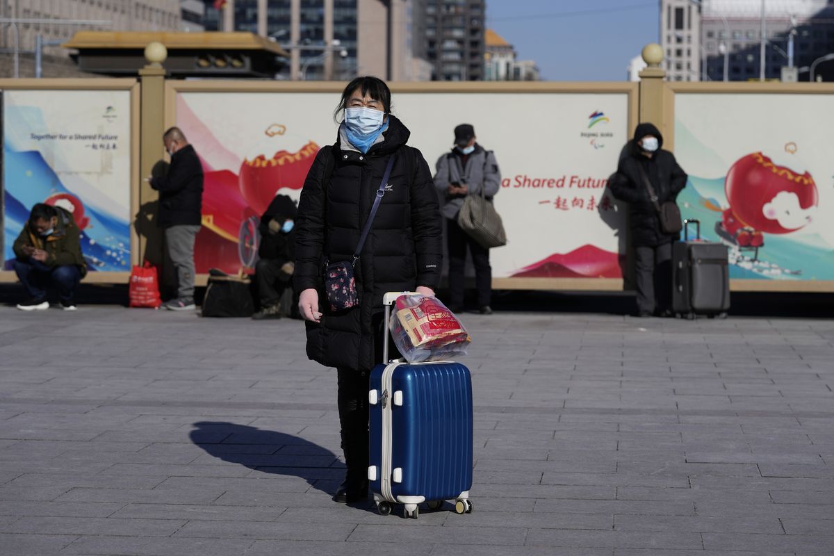 A traveler waits outside the Beijing railway station with her suitcase in Beijing, China, Friday, Jan. 28, 2022. The Beijing Winter Olympics is coinciding with the Chinese Lunar New Year and renewed Covid outbreaks prompting the Chinese authorities to call on the public to stay where they are instead of traveling to their hometowns for the year