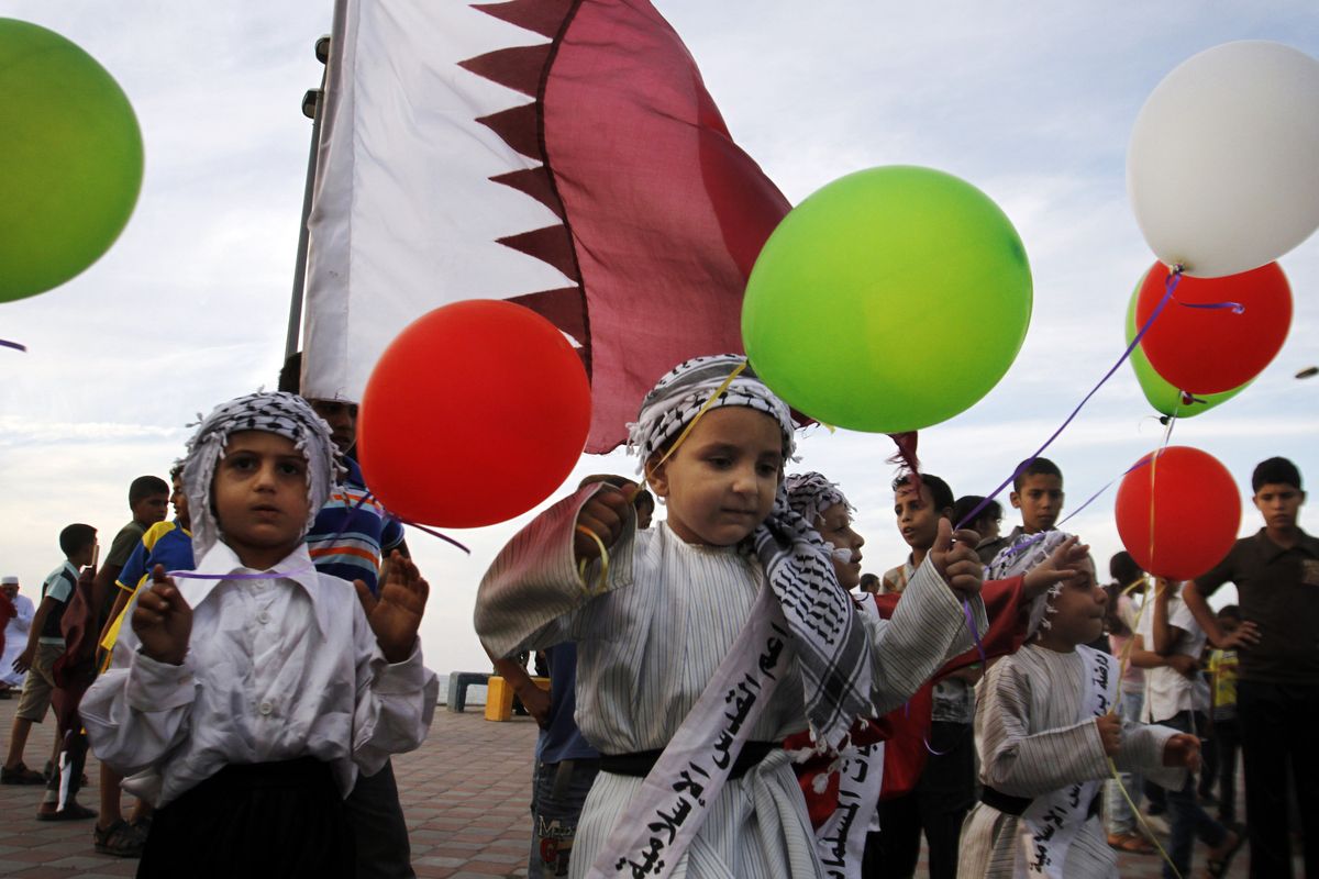 Palestinian children wave balloons and Qatari flags while waiting for the convoy of the emir of Qatar to pass by a street in Gaza City on Tuesday. (Associated Press)