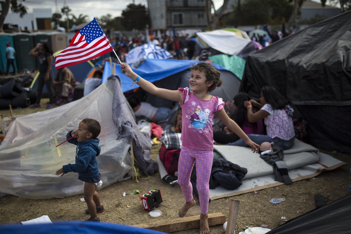 Seven-year-old Honduran migrant Genesis Belen Mejia Flores waves an American flag at U.S. border control helicopters flying overhead near the Benito Juarez Sports Center serving as a temporary shelter for Central American migrants, in Tijuana, Mexico, Saturday, Nov. 24, 2018. The mayor of Tijuana has declared a humanitarian crisis in his border city and says that he has asked the United Nations for aid to deal with the approximately 5,000 Central American migrants who have arrived in the city. (Rodrigo Abd / AP)