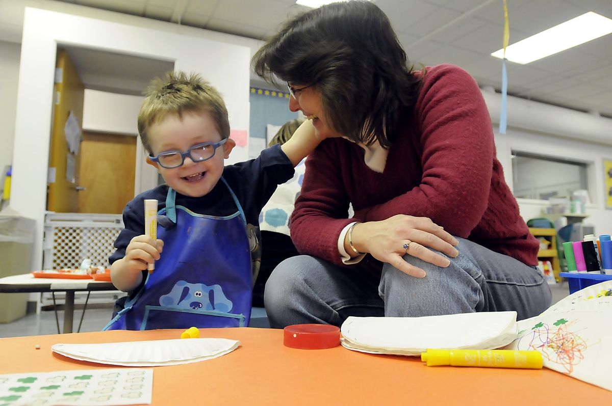 Teachers aide Lois Robertson, right, laughs with Daymien Reno-Kane about his drawing in a classroom at the Spokane Guilds’ School and Neuromuscular Center. The Guilds’ School serves children with developmental disabilities up to age 3.  (Photos by JESSE TINSLEY / The Spokesman-Review)