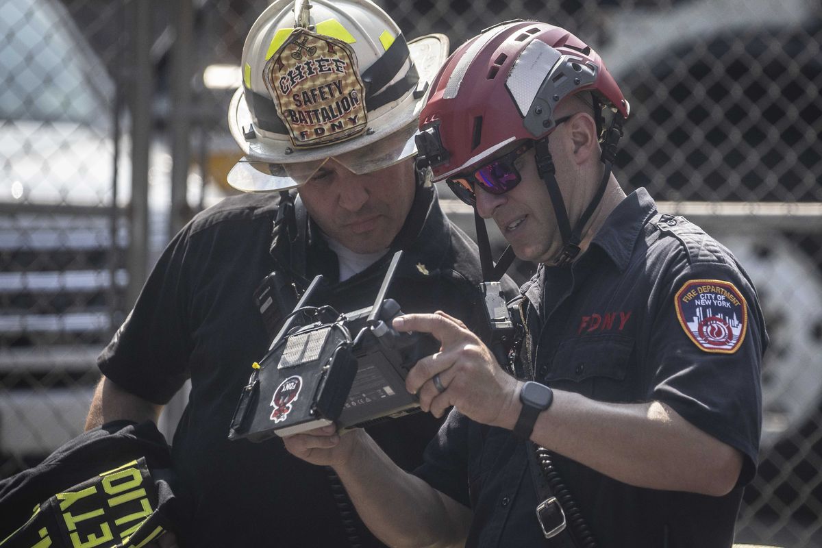 Firefighters examine a screen on a drone controller at the scene where a tower crane caught fire and partially collapsed 45 stories above the street at 550 10th Avenue in New York, July 26, 2023. Four civilians and two firefighters received minor injuries when the crane on 10th Avenue collapsed, officials said.    (Dave Sanders/The New York Times)