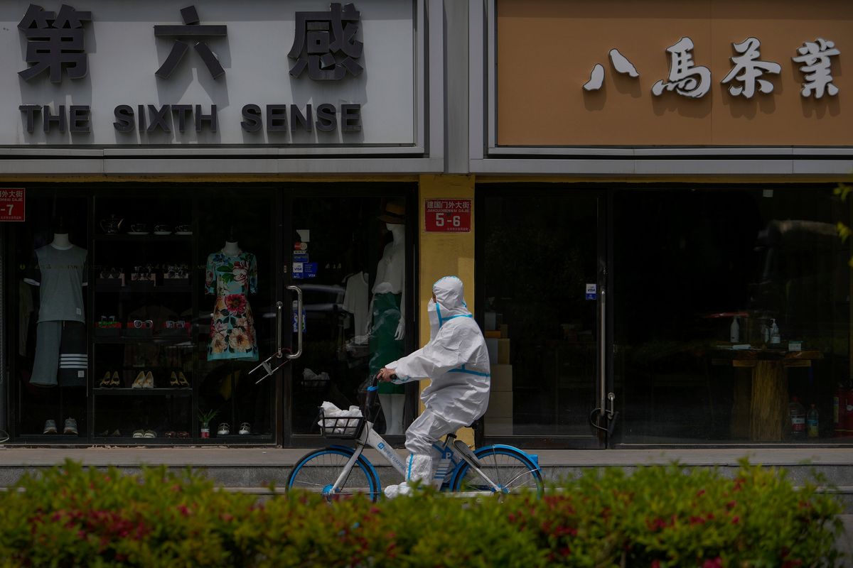 A worker in a protective suit rides a bicycle past shuttered retail shops after authorities ordered the closing down of non-essential businesses and asked people to work at home in the Chaoyang district on Monday, May 9, 2022, in Beijing.  (Andy Wong)