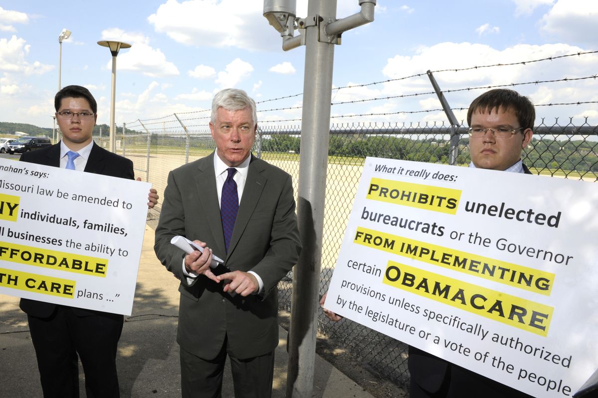 Lt. Gov. Peter Kinder on Tuesday July 10, 2012, is flanked by staff members holding signs with ballot language written by Secretary of State Robin Carnahan, left, and Kinder