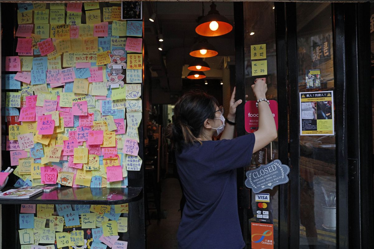 An employee removes stickers and posters with messages in support of the pro-democracy movement at a restaurant in Hong Kong, Thursday, July 2, 2020. Hong Kong police have made the first arrests under a new national security law imposed by mainland China, as thousands of people defied tear gas and pepper pellets to protest against it. Police say they arrested 10 people under the law, including at least one who was carrying a Hong Kong independence flag.  (Kin Cheung)