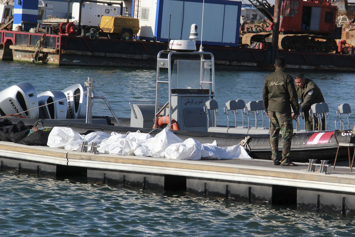 Tunisian coast guards stand next to the clovered dead bodies of migrants in the port of Sfax, central Tunisia, Thursday, Dec. 24, 2020. About 20 African migrants were found dead Thursday after their smuggling boat sank in the Mediterranean Sea while trying to reach Europe, Tunisian authorities said. Coast guard boats and local fishermen found and retrieved the bodies in the waters off the coastal city of Sfax in central Tunisia.  (Houssem Zouari)