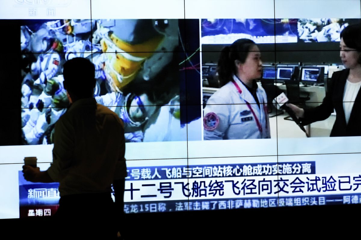 A man is silhouetted as he watches a TV screen showing CCTV broadcasting a news of Chinese astronauts sit inside the Shenzhou-12 manned spacecraft preparing to return to earth, at a shopping mall in Beijing, Thursday, Sept. 16, 2021.  (Andy Wong)