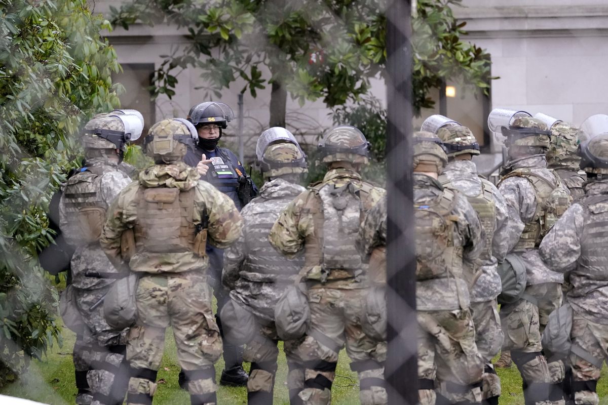 A Washington State Patrol trooper talks with members of the Washington National Guard inside a fence surrounding the Capitol in anticipation of protests Monday, Jan. 11, 2021, in Olympia, Wash. According to organizers, some protesters are unhappy the Legislature will meeting virtually and in sessions not open to the public, due to the COVID-19 pandemic, during the 2021 session which opens Monday. Washington Gov. Jay Inslee activated members of the National Guard this week to work with the Washington State Patrol to protect the Capitol campus.  (Ted S. Warren/Associated Press)