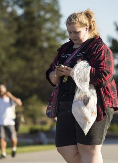 Alissa Bajramovic, of Spokane, plays ‘Pokemon Go’ as she picks up trash during a Pokemon Go community event Wednesday evening at McEuen Park. (Loren Benoit/Coeur d'Alene Press photo)