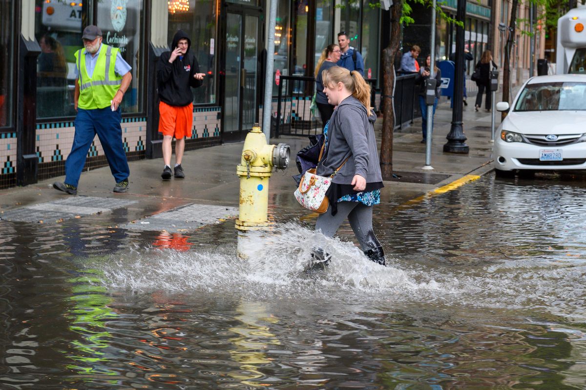 Lucky to have rain boots on, Molly Hawkins navigates the flooded intersection of Post Street and Riverside Avenue, Thurs., May 16, 20919, in downtown Spokane. (Colin Mulvany / The Spokesman-Review)