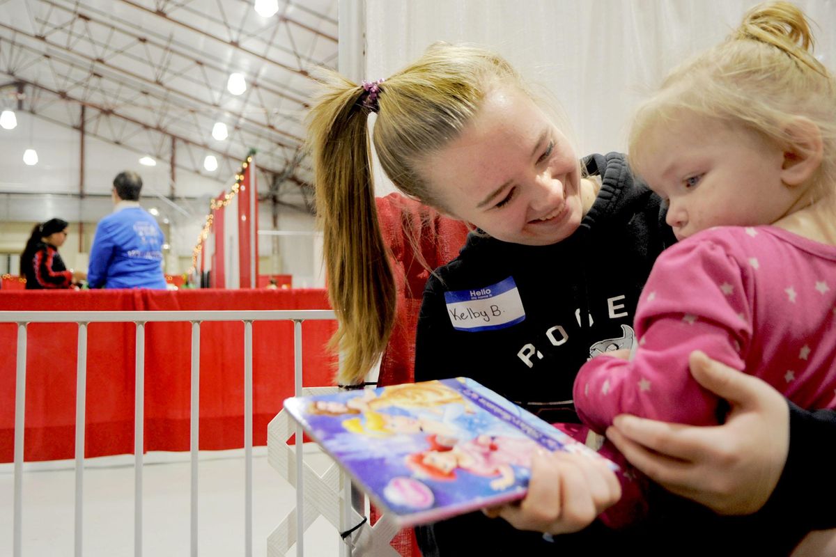 Rogers High School 11th grader Kelby Bell reads to Elaina Fields, 18-months, at the Christmas Bureau at the Spokane County Fairgrounds on Tuesday, Dec. 18, 2018. (Kathy Plonka / The Spokesman-Review)