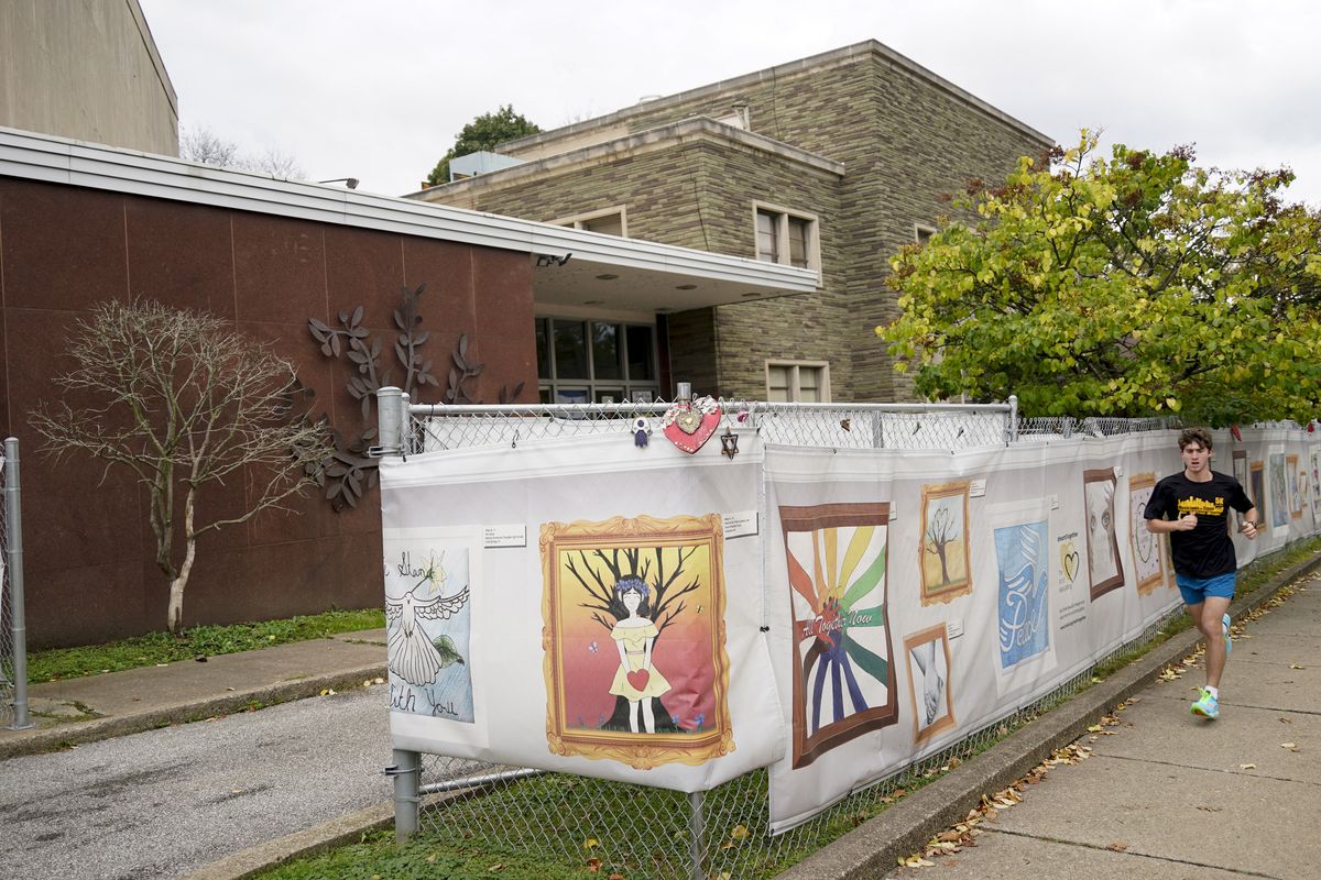 This photo from Oct. 16, 2021, shows the dormant landmark Tree of Life synagogue as a man jogs past the fencing with artwork submitted by Pittsburgh area school students in Pittsburgh