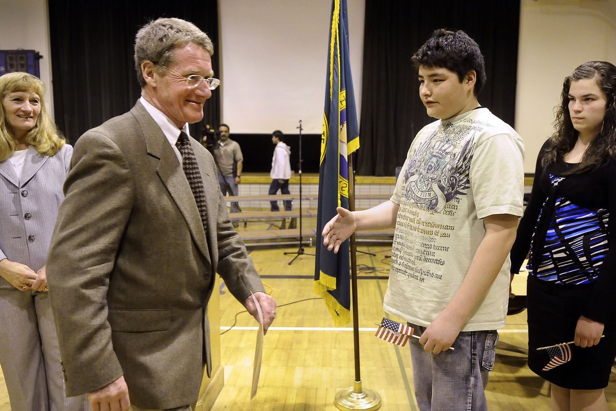 Shaw Middle School seventh-grader Raymond Skunkcap extends his hand to new U.S. citizen Norman Lewis after Lewis was presented his certificate during a naturalization ceremony Tuesday at the school. Lewis, from Scotland, arrived in this country in 1985. Students were chosen based on essays to hand out flags to the 57 new citizens. (Dan Pelle)