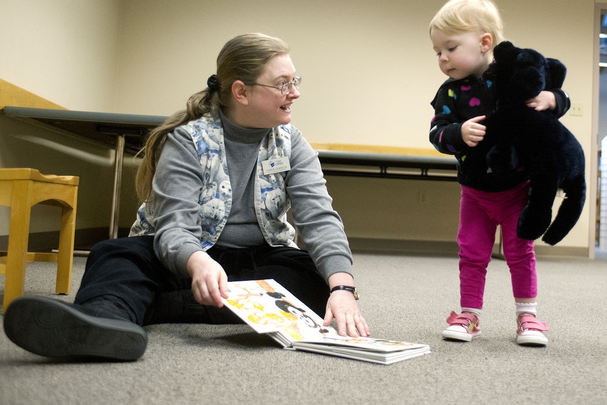 Chris LeMieux, youth services librarian, reads to Talia Arkills, 2, on Friday at the Hillyard Library. (Tyler Tjomsland)