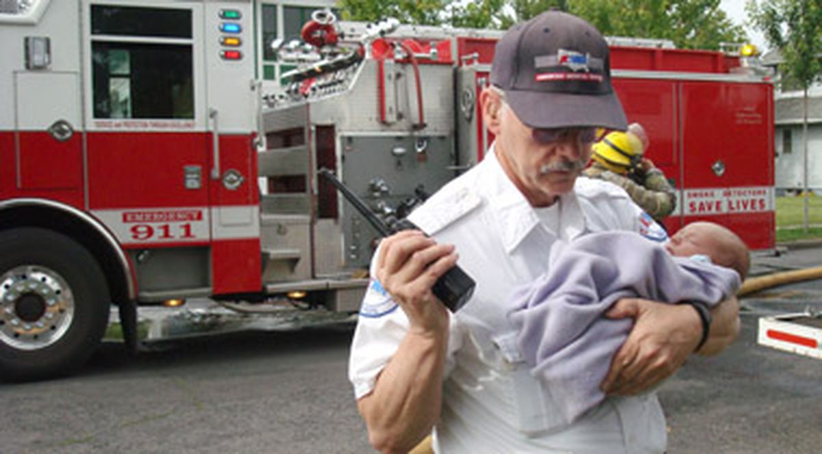 John Elser, an American Medical Response paramedic, holds 2-week-old Summerlyn Cope, whose mother, Sara Farrell, rescued her from their burning home Thursday morning. Farrell’s hair was singed, but she and her daughter weren’t injured. (John Craig)