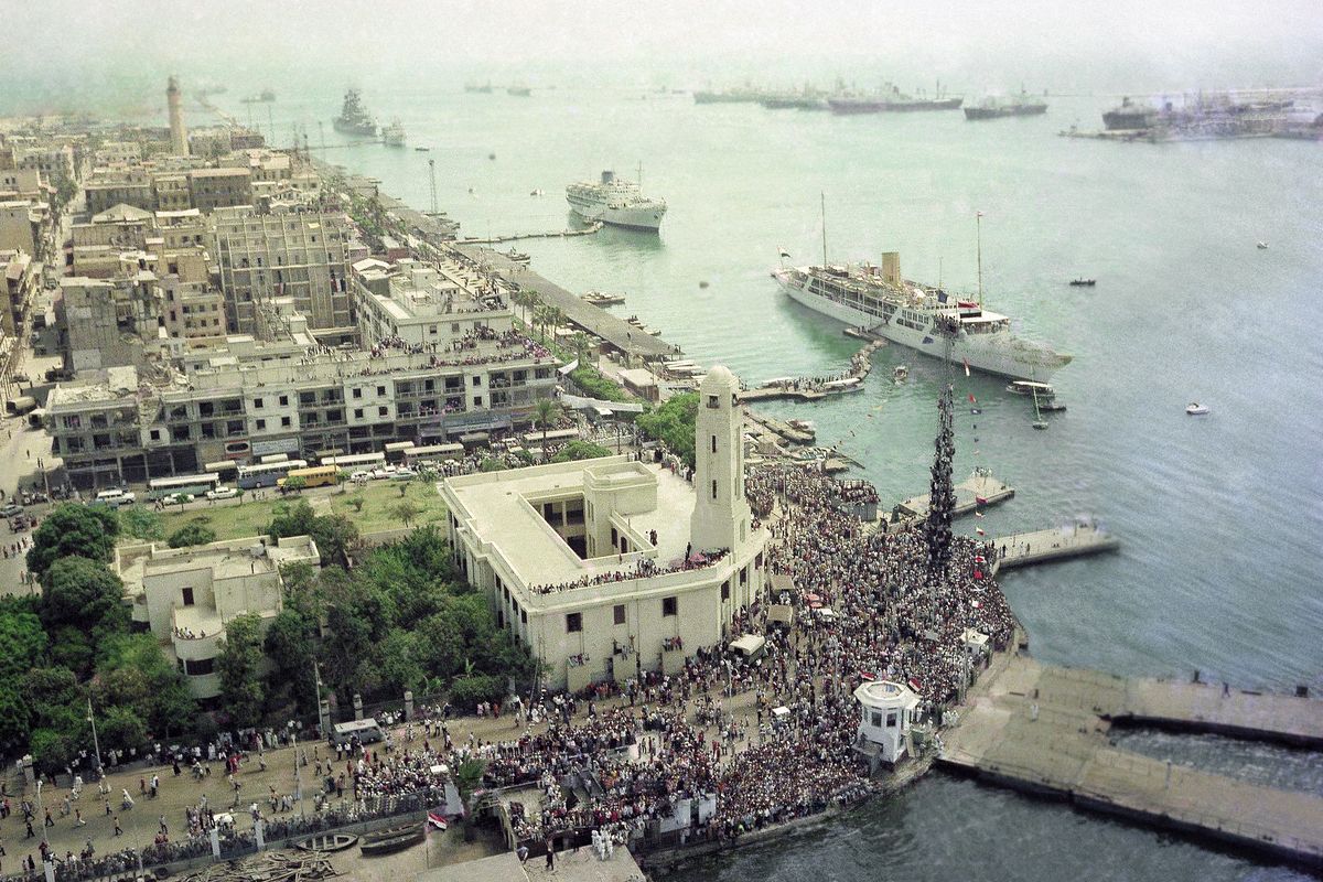 FILE - In this June 5, 1975 file photo, thousands throng the docks and quays of Port Said at the northern end of the Suez Canal in Port Said, Egypt, as the first passenger ships let off steam and pontoon ramps are kicked away as they get ready for first passage through the canal in years. Since it opened in 1869, the canal has been a source of national pride and a focus of international conflict. Now, a skyscraper-sized container ship called the Ever Given got stuck sideways across the waterway since Tuesday, March 23, 2021 . The obstruction has halted canal traffic, valued at over $9 billion a day.  (Horst Faas)