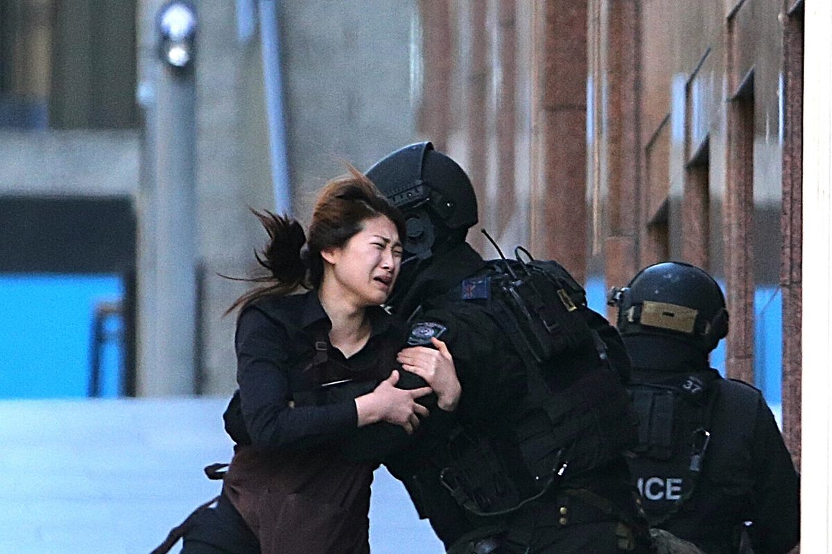 A hostage runs to armed tactical response police officers for safety after she escaped from a cafe under siege at Martin Place in the central business district of Sydney today. (Associated Press)