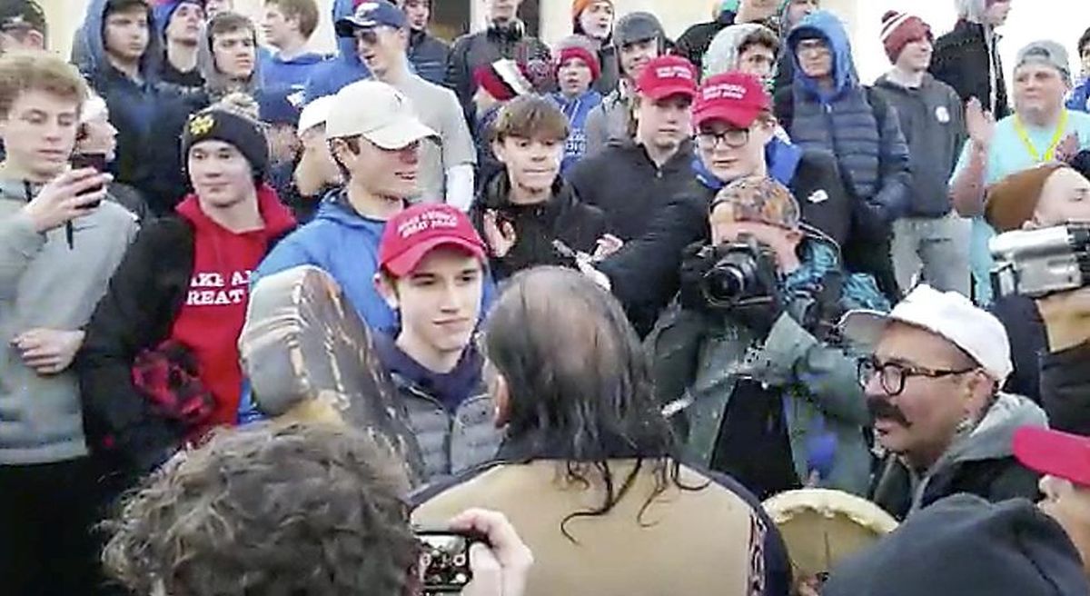 In this Friday, Jan. 18, 2019, image made from video provided by the Survival Media Agency, a teenager wearing a “Make America Great Again” hat, center left, stands in front of an elderly Native American singing and playing a drum in Washington. The Roman Catholic Diocese of Covington in Kentucky is looking into this and other videos that show youths, possibly from the diocese’s all-male Covington Catholic High School, mocking Native Americans at a rally in Washington. (AP)