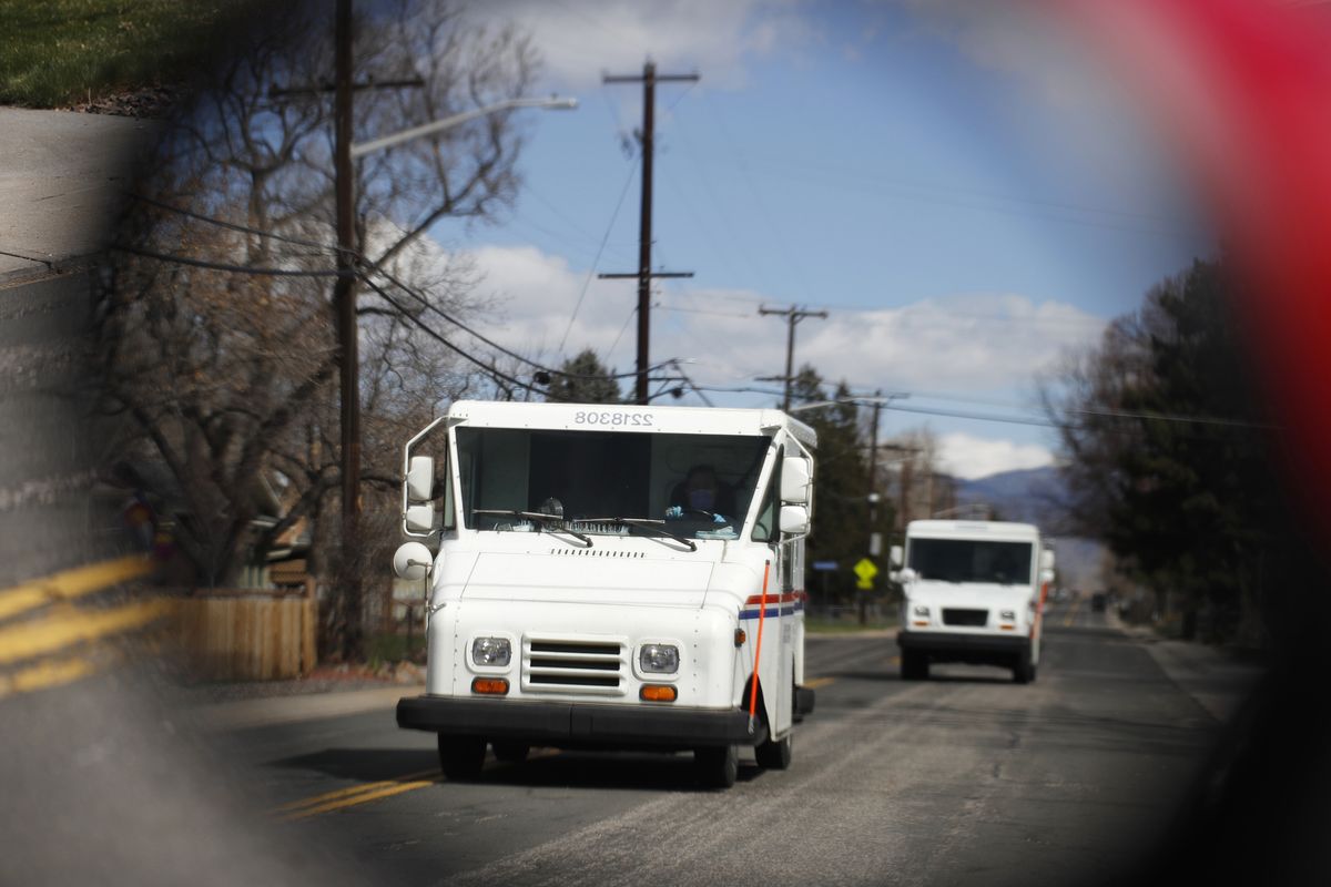 FILE - In this March 31, 2020, file photo United States Post Office delivery trucks are reflected in the side mirror of a vehicle as postal delivers set off on their daily rounds in Arvada, Colo. The U.S. Postal Service is warning states that it cannot guarantee all ballots cast by mail for the November election will arrive in time to be counted, even if mailed by state deadlines.  (David Zalubowski)