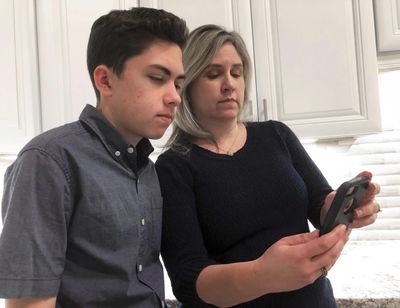 Grant Thompson and his mother, Michele, look at an iPhone in the family's kitchen in Tucson, Ariz., on Thursday, Jan. 31, 2019. Apple credited the Tucson teenager, Grant Thompson, for discovering the FaceTime bug. (Associated Press)