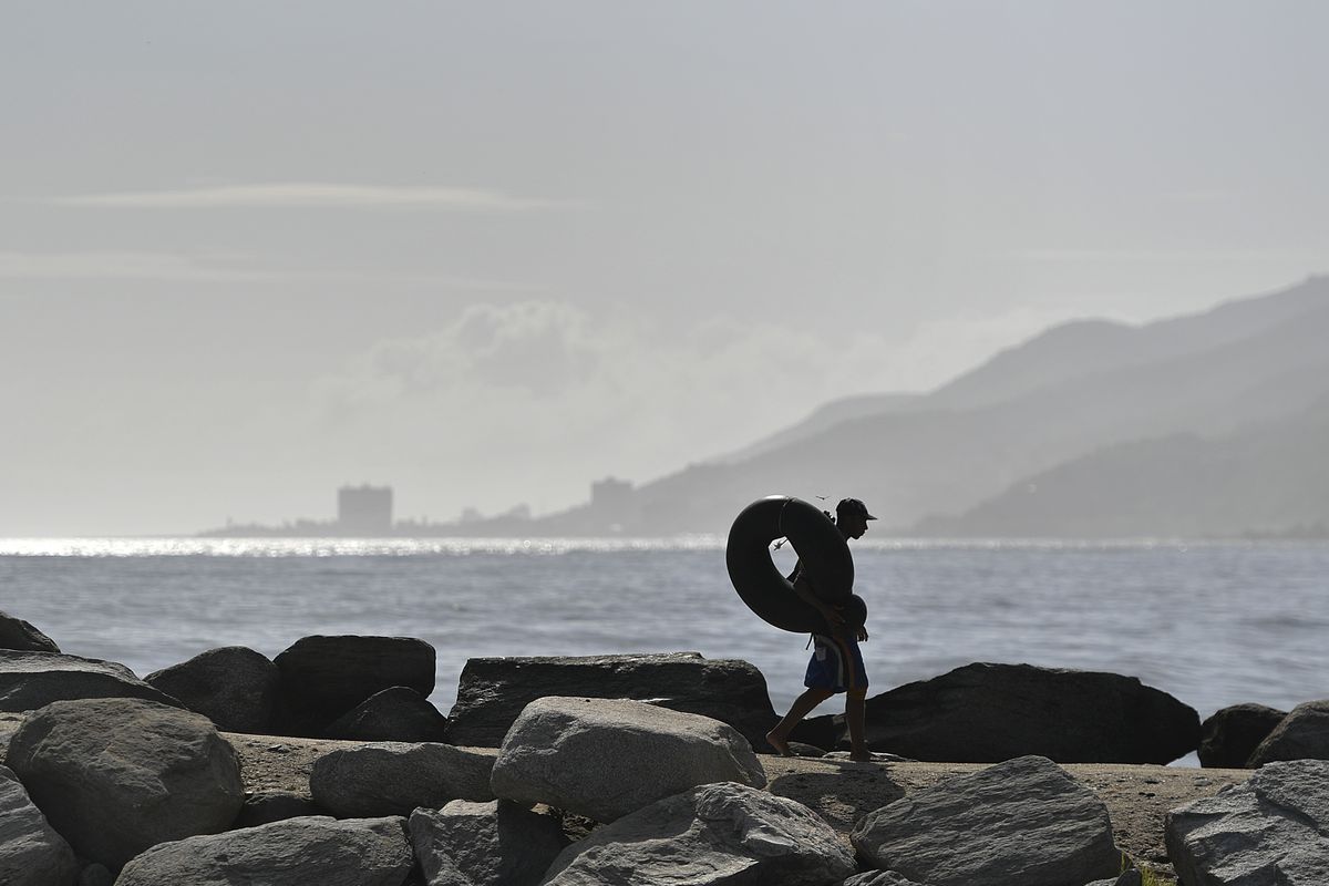Edward Murat, 20, carries his inner tube to the beach for a day of open sea fishing Friday at Playa Escondida in La Guaira, Venezuela.  (Matias Delacroix)