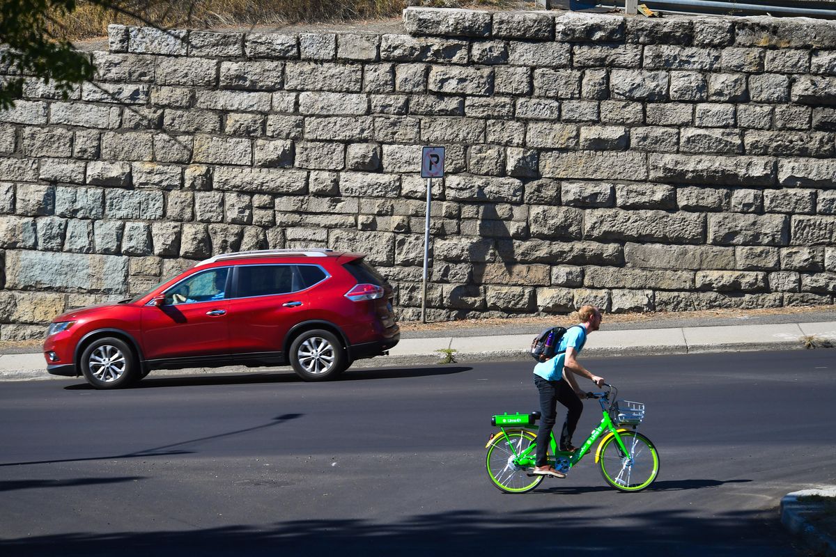 James Burgess, 25, rides a Lime bike north up North Monroe Street near the retaining wall Friday. Before 1929, the granite blocks in the wall were part of the old Granite Building downtown, where the Paulsen building now stands. (Dan Pelle / DAN PELLE/The Spokesman-Review)