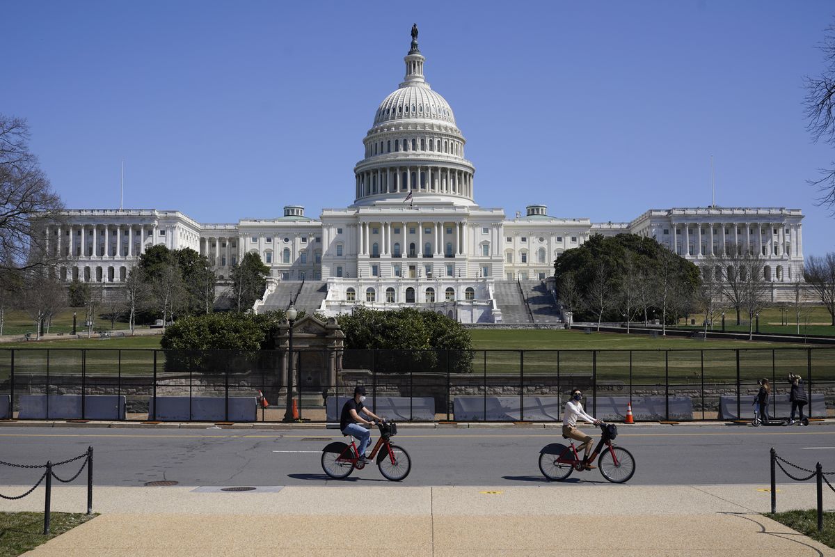 Bicyclists ride past an inner perimeter of security fencing on Capitol Hill in Washington, Sunday, March 21, 2021, after portions of an outer perimeter of fencing were removed overnight to allow public access.  (Patrick Semansky)