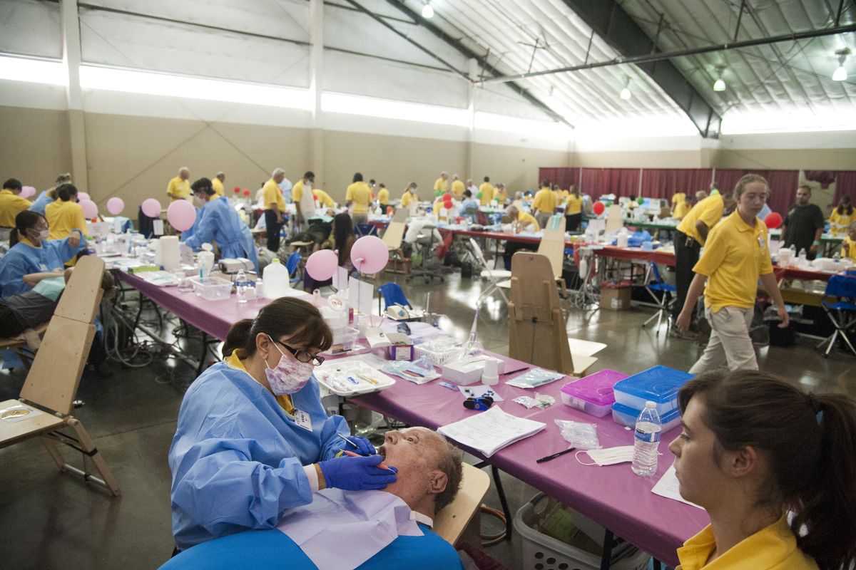 Volunteer dental hygienist Vicki Dye, left, of Sandpoint, begins a cleaning on patient Ralph White in the dental care area Monday at the Spokane Fair and Expo Center, the site of the Your Best Pathway to Health clinic coordinated by the Seventh-day Adventist Church and involving many donors, sponsors and volunteers. At right is volunteer assistant Natalie Harder, 17. (Jesse Tinsley)