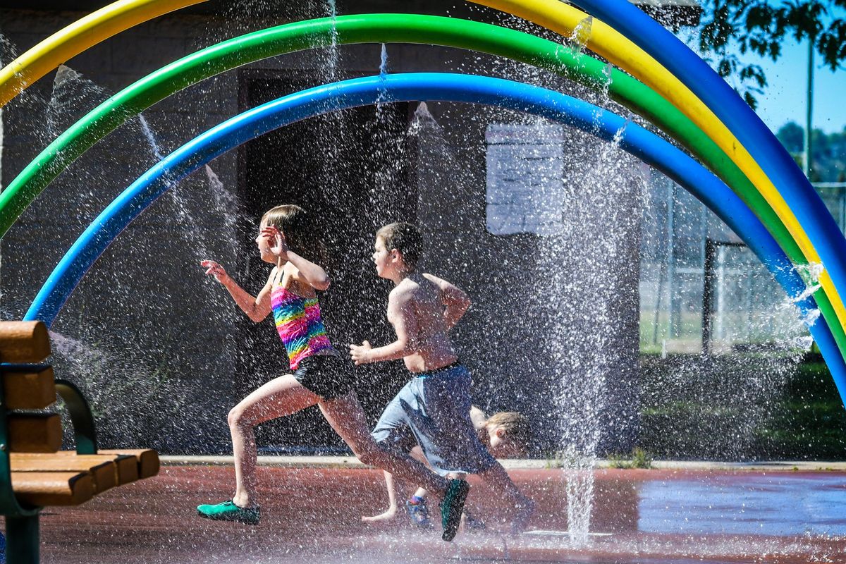 Olivia Helling, 7, and Adrian Compton, 10, sprint their way through the Franklin Park splash pad spray June 6, 2023, in Spokane.  (Spokesman-Review photo archives)