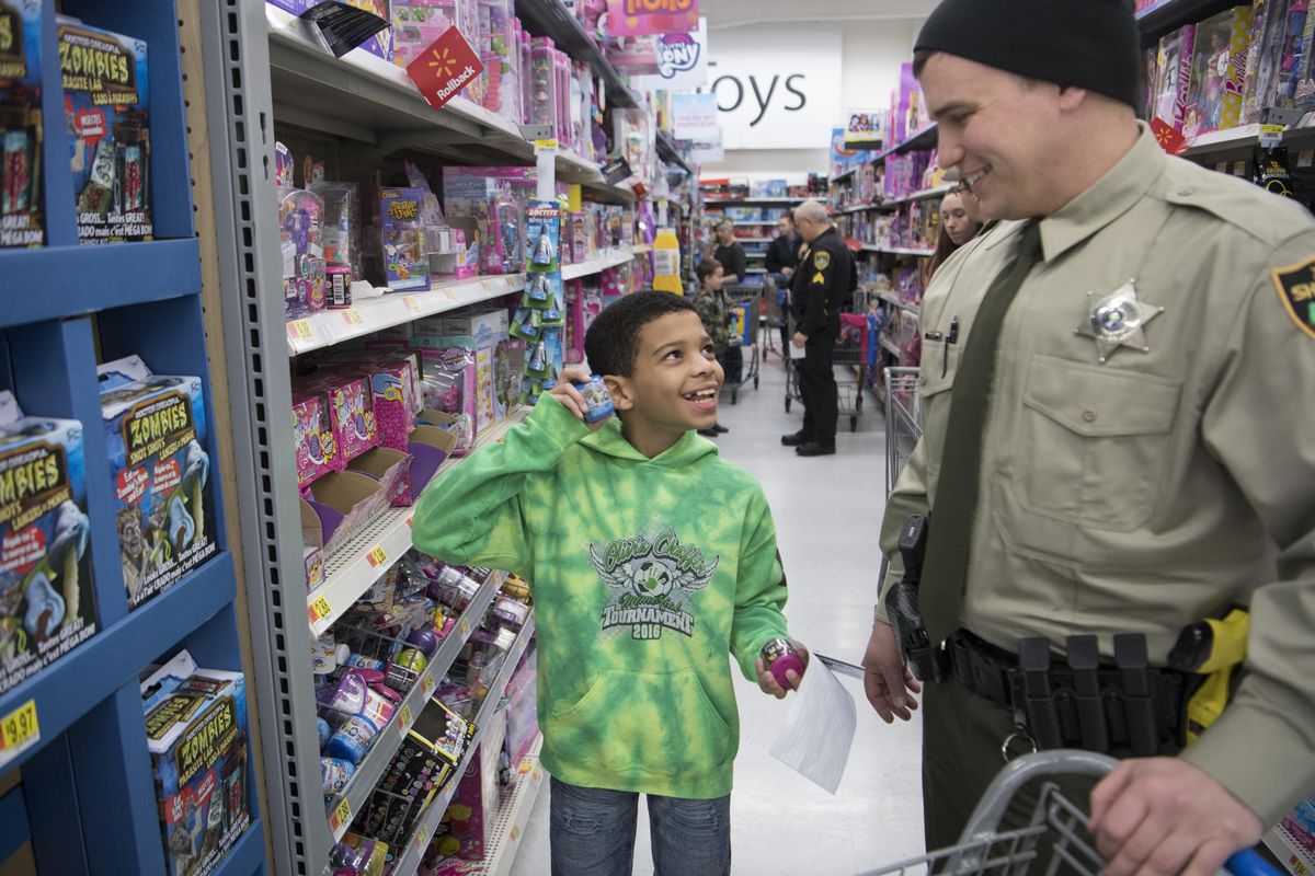 Michael Jerome Sanders, left, shakes a toy that makes the sound of laughing while shopping with Spokane County Sheriffs Deputy Dan Moman, right, during a Holiday and Heroes event at the Walmart in Spokane Valley at 15727 East Broadway Ave. Sunday, Dec. 10, 2017. (Jesse Tinsley / The Spokesman-Review)