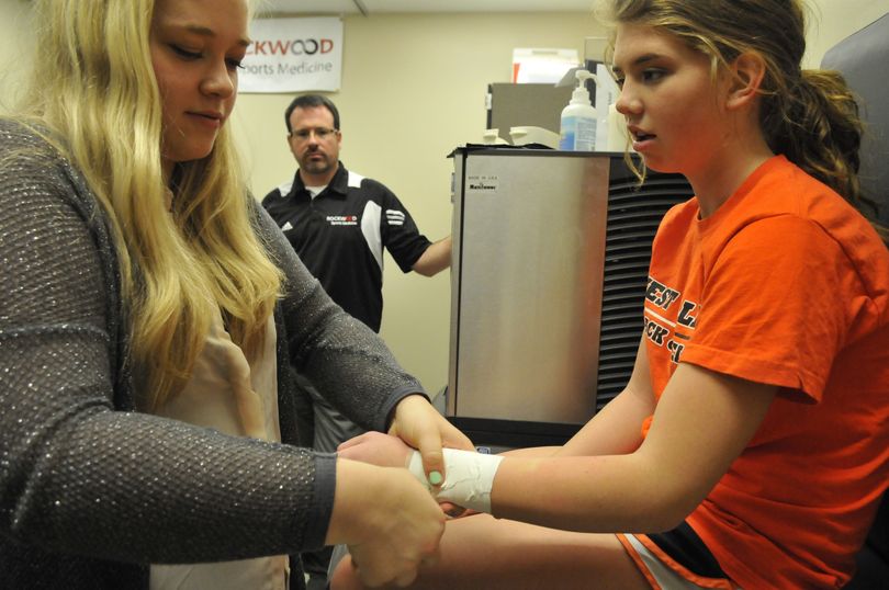 West Valley senior Corbin Smith, left, tapes the wrist of sophomore cheerleader Kensley Seacrest under the watchful eye of sports medicine instructor Keith Eggleston at West Valley High School on Tuesday. (Jesse Tinsley)