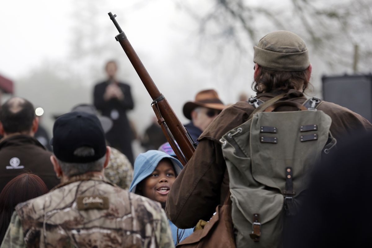 A child looks at a man carrying a rifle during a rally by gun-rights advocates to protest a new expanded gun background check law in Washington state Saturday, Dec. 13, 2014, in Olympia, Wash. Saturday