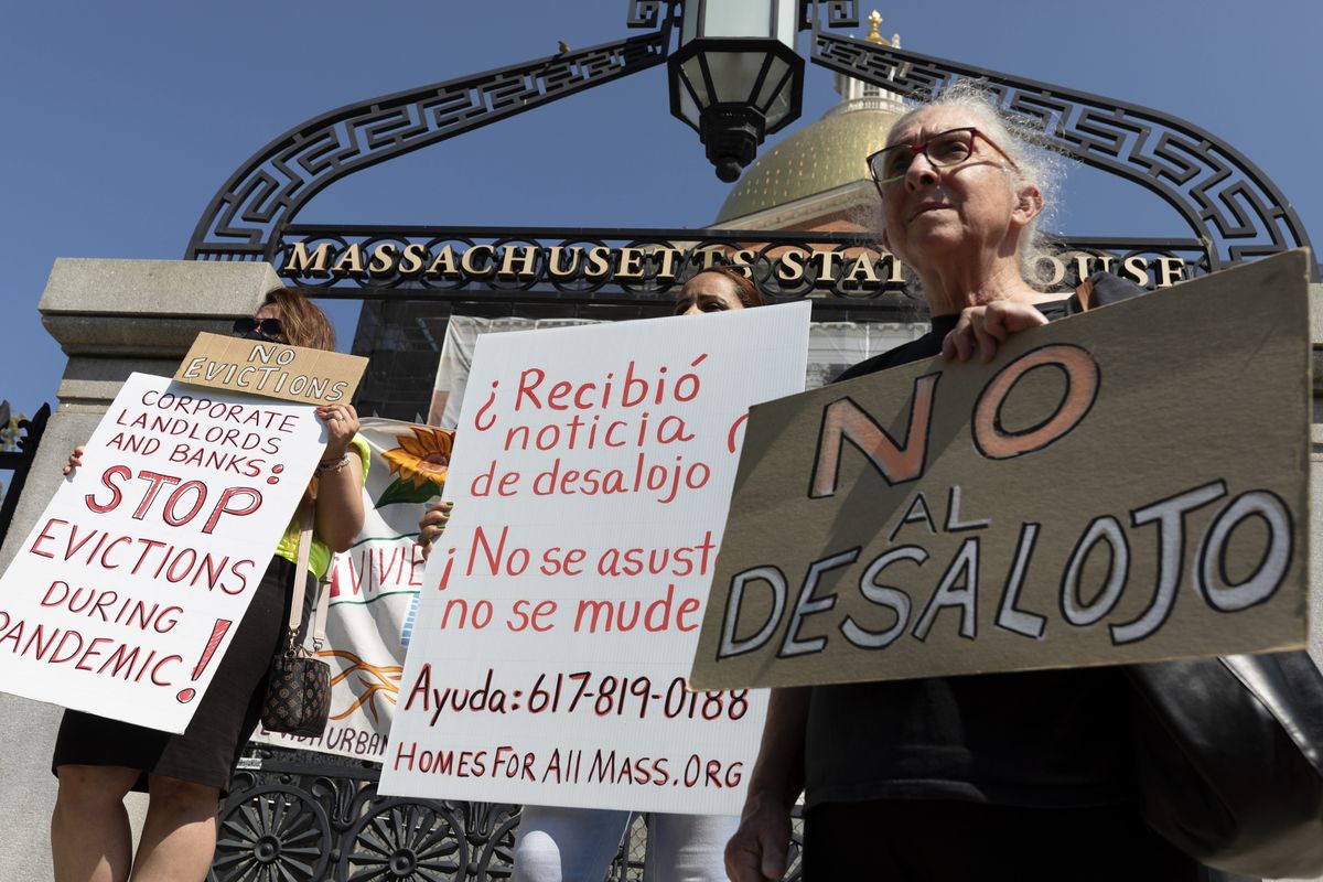 People from a coalition of housing justice groups hold signs protesting evictions during a news conference outside the Statehouse on Friday in Boston.  (Michael Dwyer)