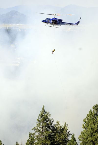 Fire battle: A member of the Coeur d’Alene Helitack crew from the Idaho Department of Lands rappels out of a helicopter to a spot near a wildland fire south of the Post Falls Dam along the Spokane River on Monday. The fire covered two to three acres of a natural area used mainly for hiking. (Jesse Tinsley)