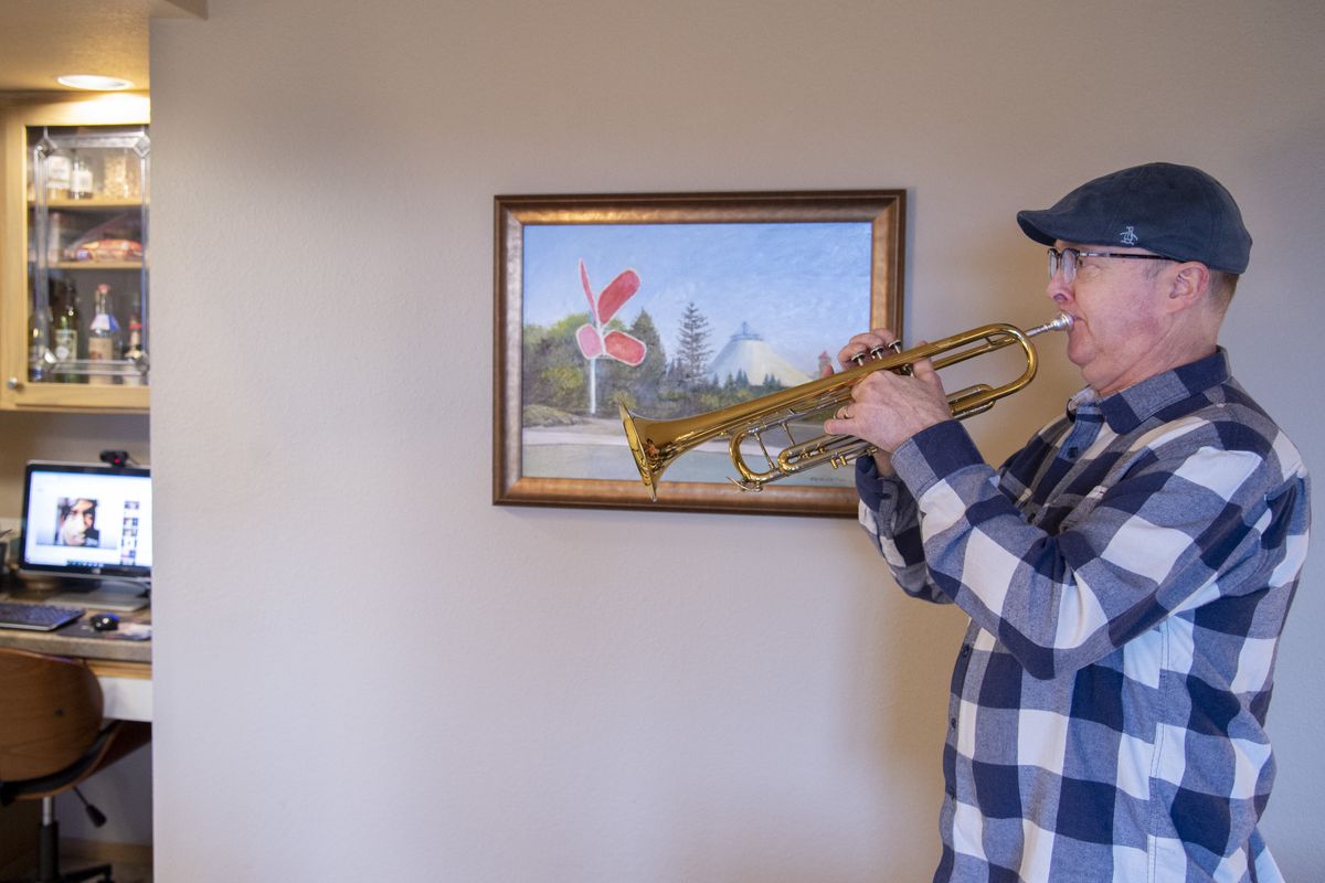 Trumpeter Chris. Cook, right, plays along with a song playing on his computer while being filmed by his daughter Kelsey, no shown, in his Spokane apartment Thursday, Jan. 7, 2021. Kelsey, a stand-up comedian, has started a series of Instagram videos of her dad, a Spokane Symphony brass player, playing along with pop hits and the two are continuing the series as a pandemic project because of the popularity.  (Jesse Tinsley/The Spokesman-Review)