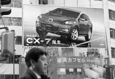 
A man walks underneath a billboard for the Mazda CX-7 in Tokyo. 
 (Associated Press / The Spokesman-Review)