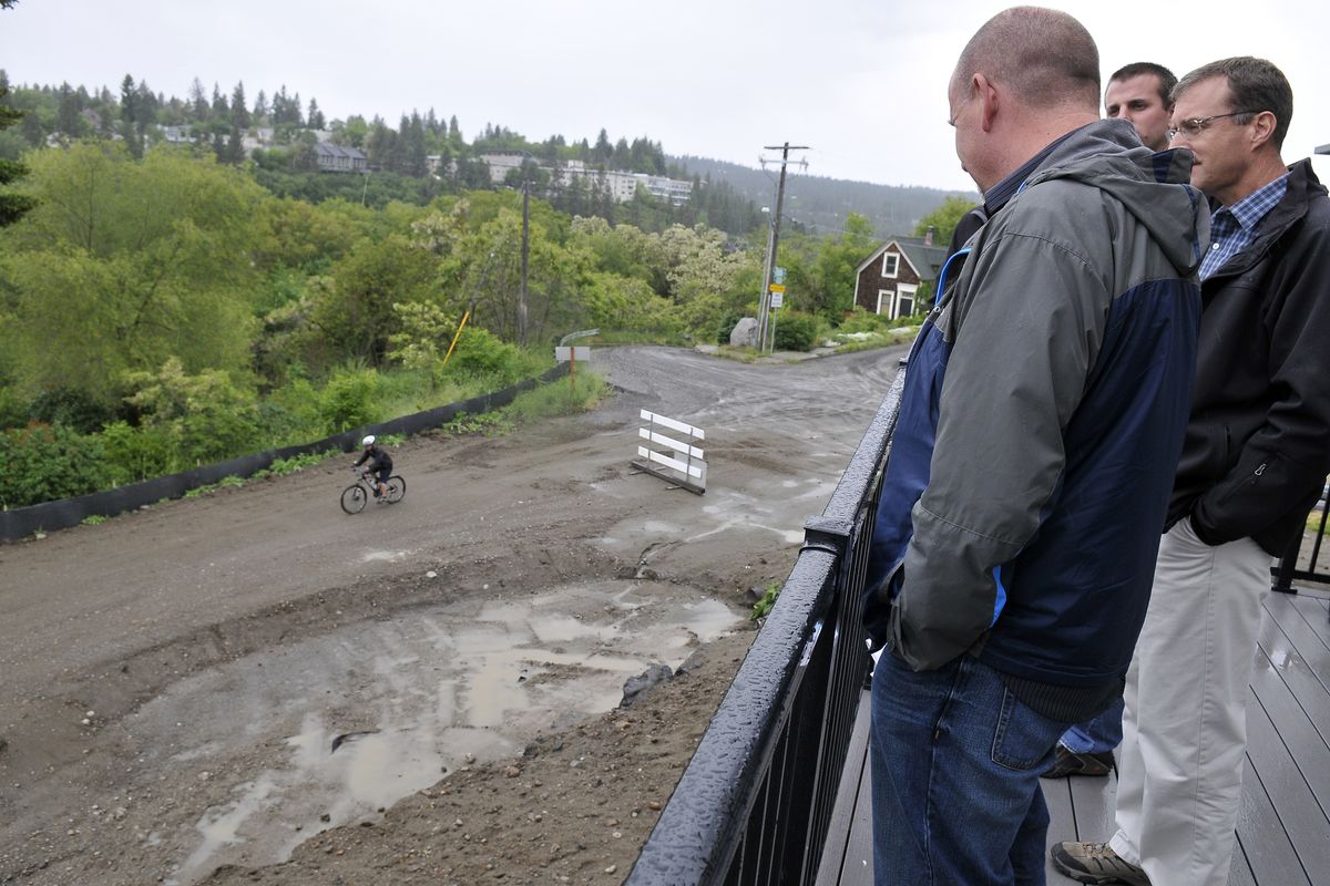 A mountain biker rides along the roughly graded section of the Centennial Trail while visitors look down from a new townhome at Kendall Yards on Wednesday. At far right (in glasses) is Michael Terrell, the landscape architect for the trail project. Greenstone Corp., which is building the homes at Kendall Yards, celebrated the final plan Wednesday for the two miles of trail from Monroe Street to the end of Kendall Yards to the west. (Jesse Tinsley)