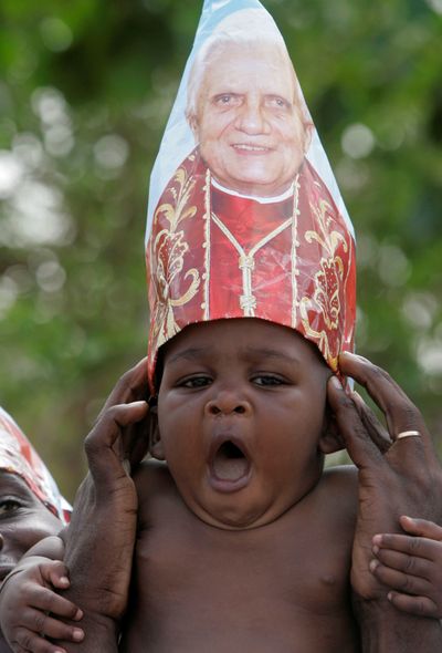 A baby wearing a hat bearing the likeness of Pope Benedict XVI is among the crowd gathered  at the airport in Luanda, Angola, for the pope’s departure Monday.  (Associated Press / The Spokesman-Review)